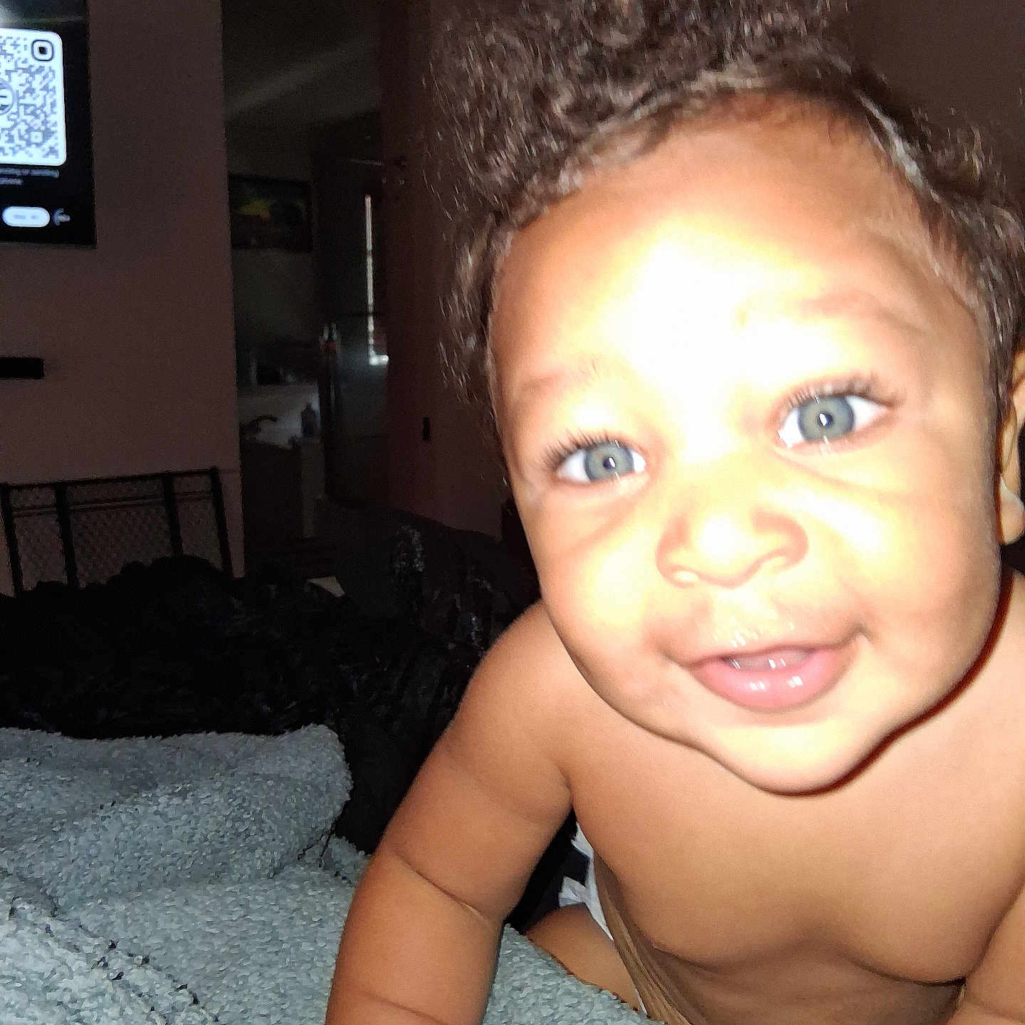 Saleem is registered to the contest to win money with this photo: arm, baby, blanket, blue_eyes, child, close_up, curly_hair, cute, diaper, face, furniture, happy, indoor, infant, person, portrait, qr_code, skin, smiling, television