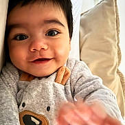 Gabin a rejoint le concours — aidez-le/la à gagner de superbes lots ! baby, child, smiling, close_up, face, hand, pillow, indoor, cute, infant, cozy, clothing, portrait, happy, young, person, soft, expression, baby_outfit, reaching