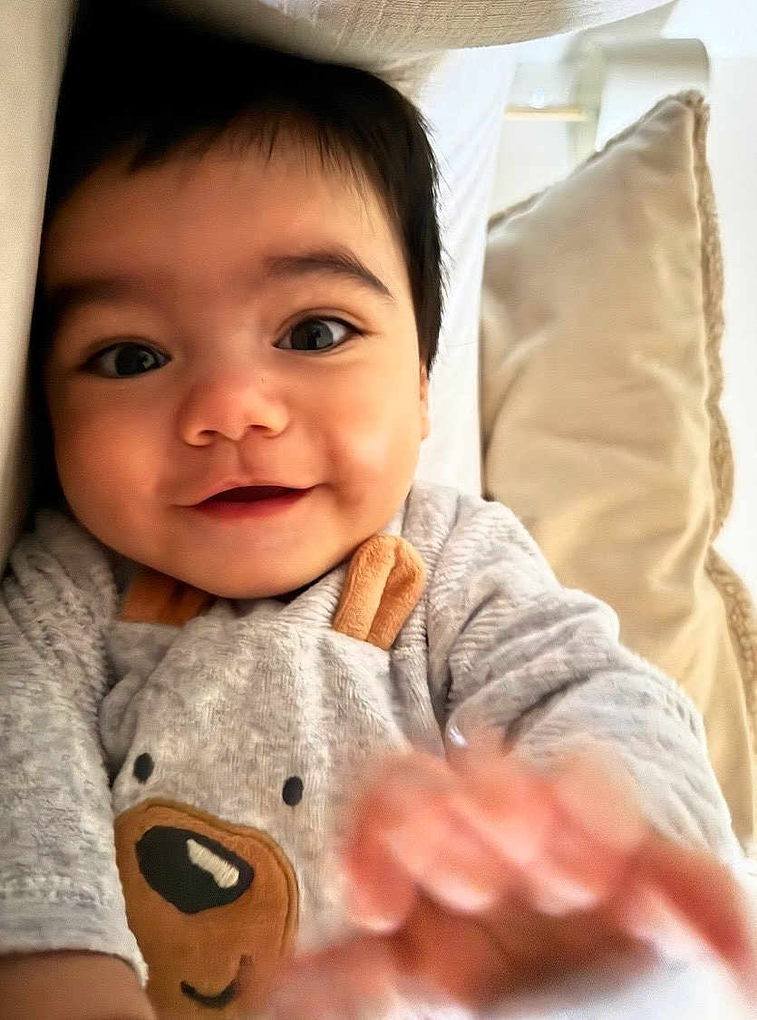 Gabin a rejoint le concours — aidez-le/la à gagner de superbes lots ! baby, child, smiling, close_up, face, hand, pillow, indoor, cute, infant, cozy, clothing, portrait, happy, young, person, soft, expression, baby_outfit, reaching