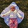 baby, child, grass, blanket, smile, happy, outdoor, clothing, jacket, pants, socks, person, infant, portrait, nature, sunlight, cute, young_child, lying_down, warm_light