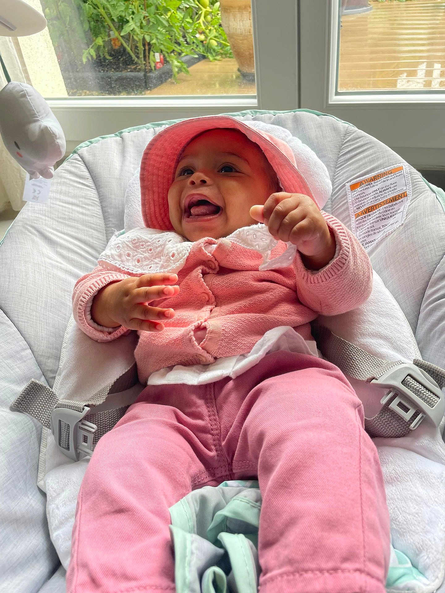 Luna a rejoint le concours — aidez-le/la à gagner de superbes lots ! baby, infant, smiling, happy, pink_clothing, hat, baby_seat, indoor, window, natural_light, cute, child, playful, comfortable, cushion, hands, face, person, home, joy