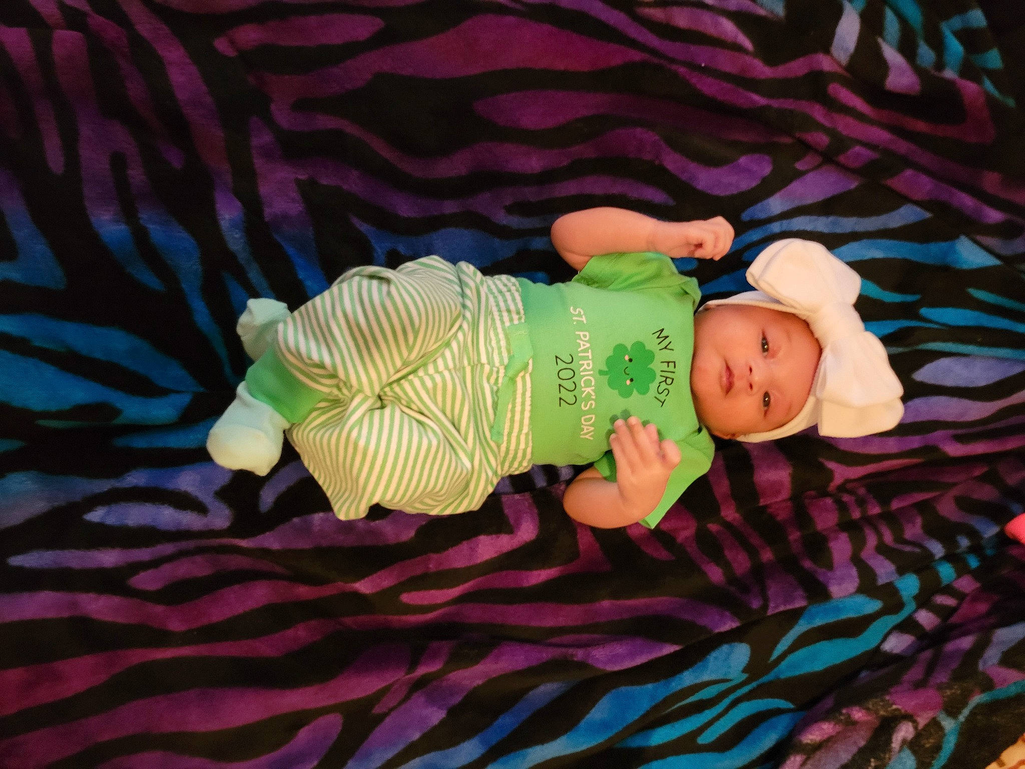 Leila is registered to the contest to win money with this photo: baby, baby_products, baby_toddler_clothing, cap, child, doll, fashion_accessory, finger, grass, hat, linens, pattern, person, purple, textile, toddler, toy