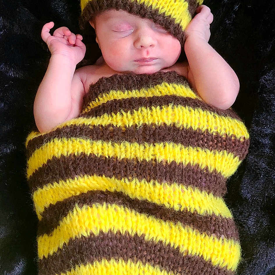 Luella is registered to the contest to win money with this photo: baby, baby_toddler_clothing, cap, cheek, eye, face, hand, head, headgear, human_body, knit_cap, outerwear, plant, sleeve, t_shirt, textile, toddler, tree, woolen, yellow