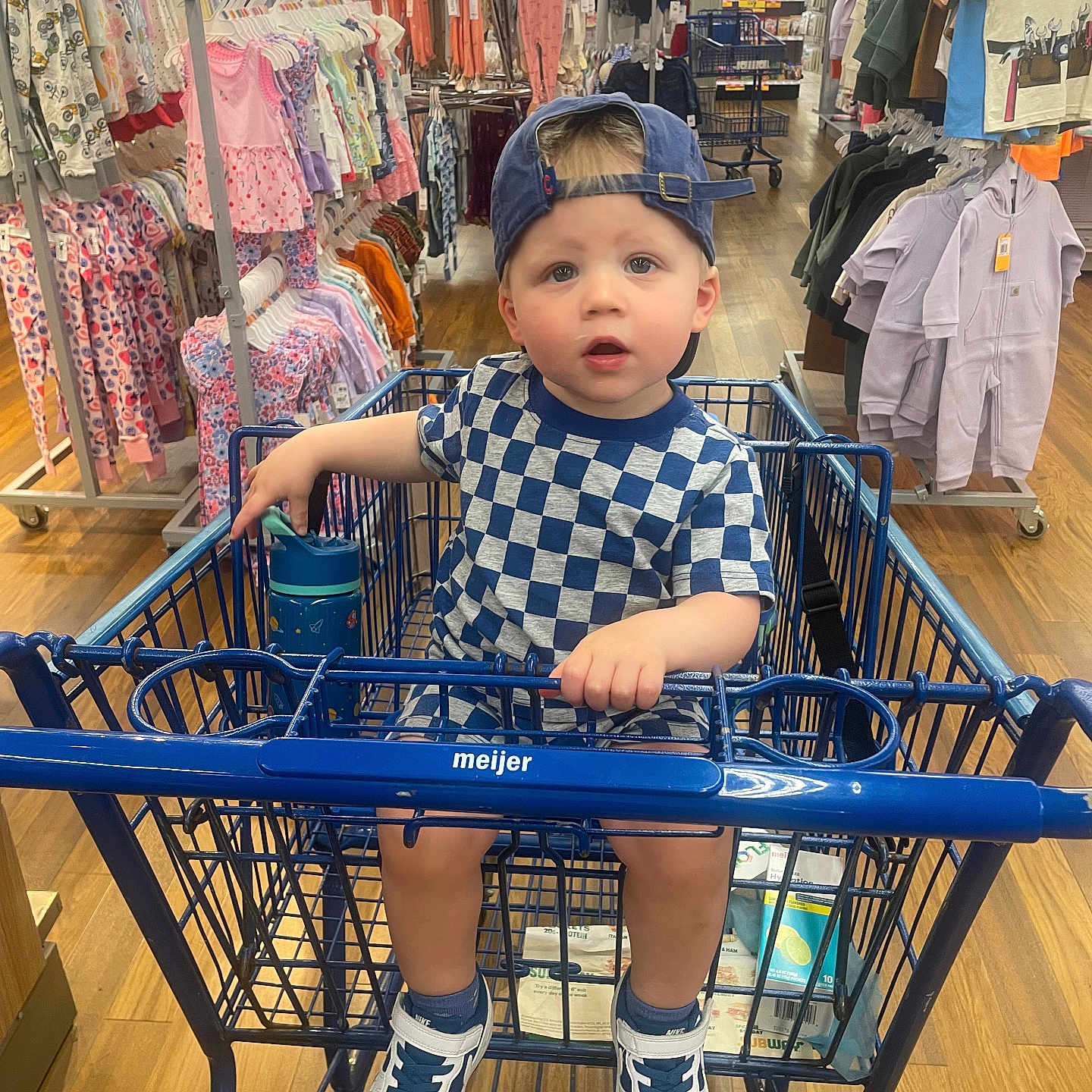 Sawyer is registered to the contest to win money with this photo: aisle, baby, baby_clothes, backwards_cap, blue, checkerboard_shirt, child, clothing_store, curious, family_outing, indoors, portrait, retail, shopping, shopping_cart, sitting, smiling, sneakers, supermarket, toddler