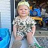 baseball_cap, blue, brick_wall, child, dinosaur_clothing, dinosaur_shirt, garage, gravel, happy, outdoors, playhouse, playtime, portrait, ride_on_toy, shorts, sitting, smiling, sneakers, toddler, toy_vehicle