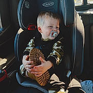 Sawyer joined the competition — help win amazing prizes! automobile, baby, blond_hair, boots, buckled_in, camouflage_clothing, car_seat, child, hands, indoors, pacifier, portrait, safety_harness, shoe_sole, sitting, smiling, sunlight, toddler, vehicle, window
