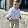 toddler, child, boy, street, urban, sidewalk, pavement, white_shirt, khaki_pants, blue_shoes, confident, sunny, daylight, walking, building, window, casual_clothing, pose, smile, person