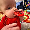 baby, chewing, child, closeup, colorful, cute, face, floor, hand, head, indoor, infant, person, play_area, play_mat, red_shirt, seated, striped_pants, toy, young_child