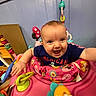 activity_center, baby, blue_shirt, child, colorful, cute, expression, face, happy, indoor, infant, person, pink, plastic_toys, playtime, seat, smiling, toys, wooden_wall, young_child
