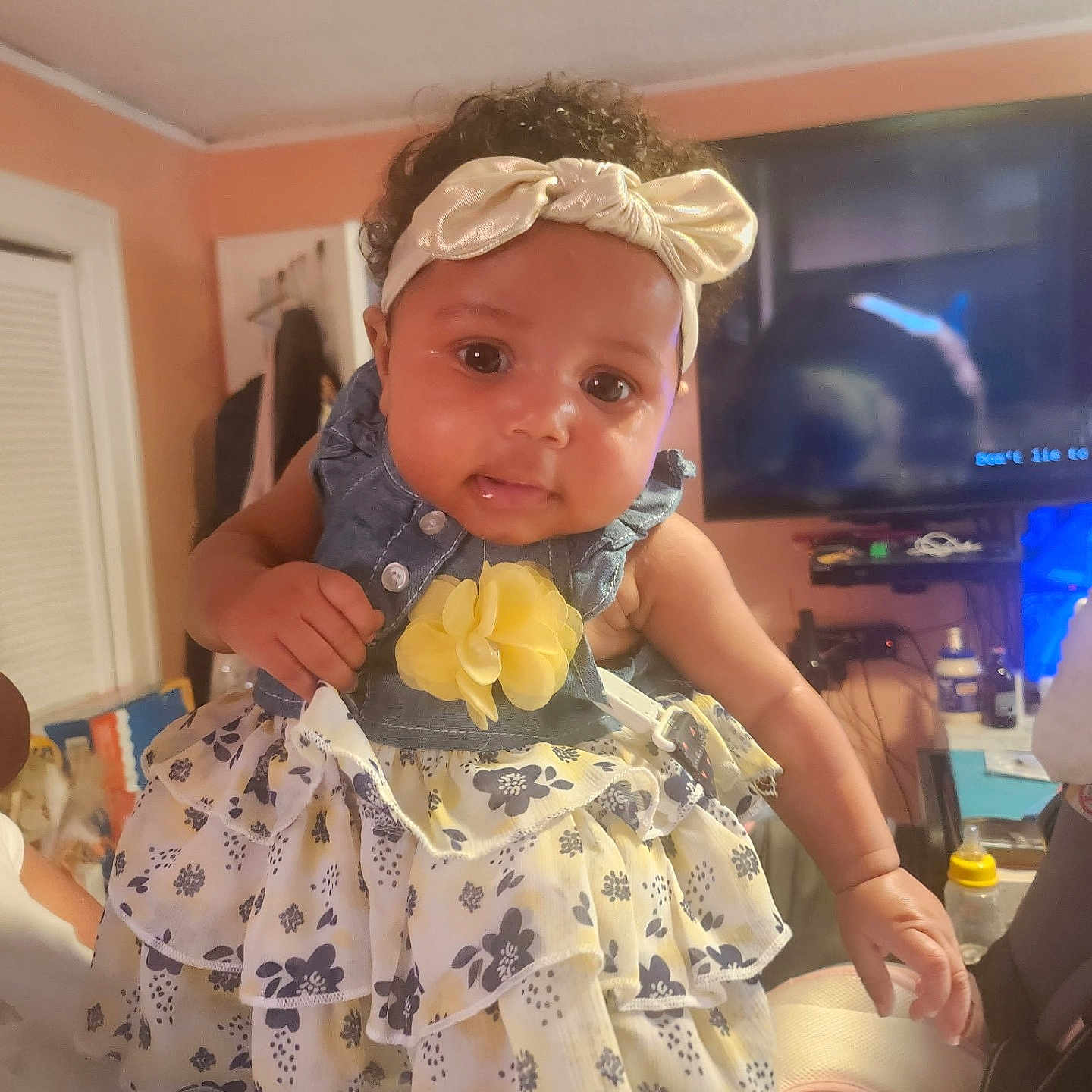Ta'Lanni joined the competition — help win amazing prizes! baby, bottle, child, clothing, curly_hair, cute, dress, face, flower, furniture, hand, headband, holding, indoor, infant, person, portrait, room, smiling, television