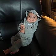 Jeremiah joined the competition — help win amazing prizes! baby, smiling, hoodie, gray_clothing, nike, infant, leather_couch, indoor, cozy, happy, child, person, casual, relaxed, comfort, living_room, candid, portrait, small_hands, barefoot