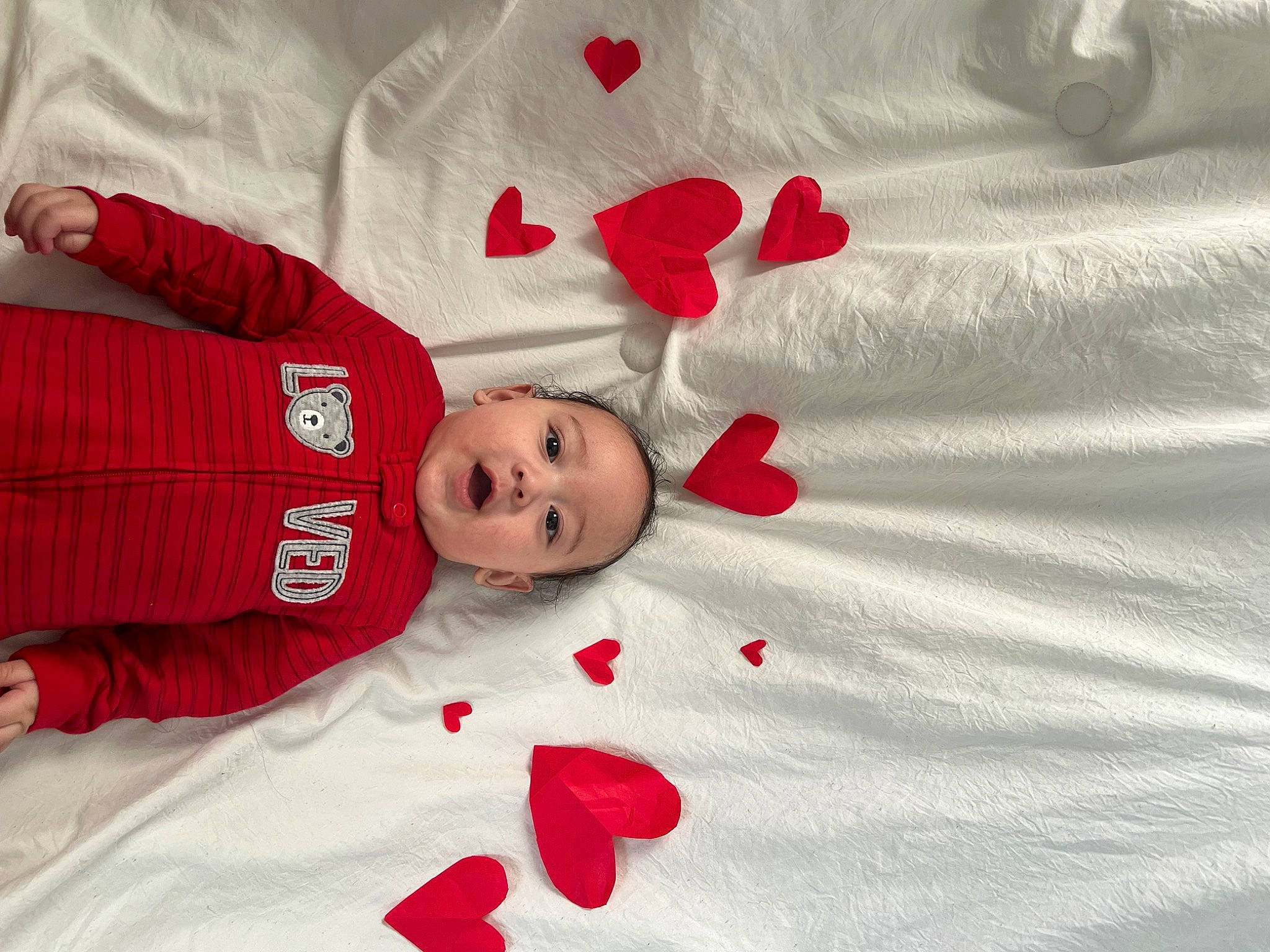 Derrick is registered to the contest to win money with this photo: baby, baby_toddler_clothing, bed_sheet, bedding, carmine, child, comfort, event, eye, fur, happy, linens, pattern, person, petal, red, room, sleeve, smile, textile