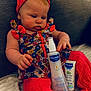 baby, infant, child, floral_dress, red_headband, red_leggings, mustela_products, bottle, tube, sofa, blanket, indoor, curious, sitting, skin_care, person, face, hand, cozy, cute