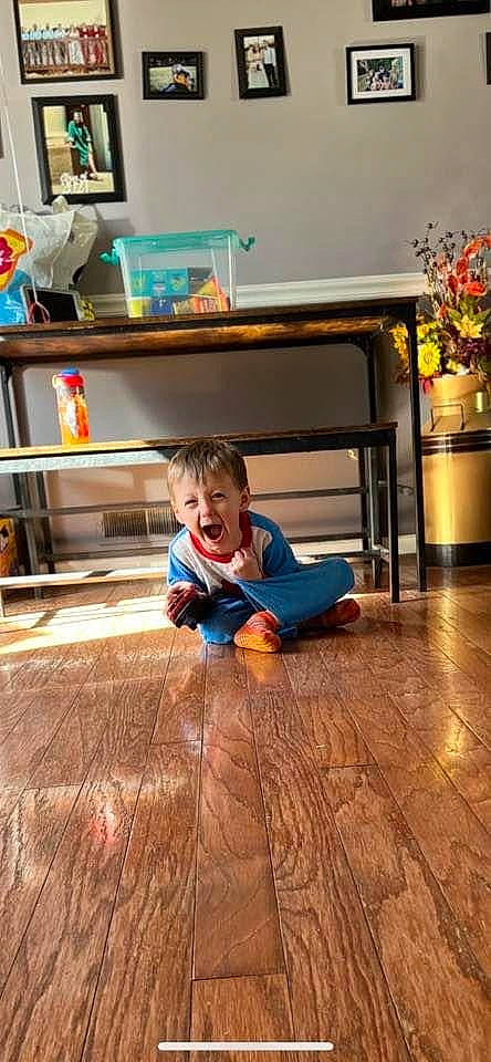 Thomas is registered to the contest to win money with this photo: baby_toddler_clothing, chair, child, comfort, desk, floor, flooring, hardwood, house, houseplant, laminate_flooring, person, picture_frame, plant, smile, table, toddler, varnish, wood, wood_flooring