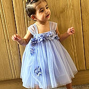 Avleen is registered to the contest to win money with this photo: toddler, child, dress, purple_dress, flowers, barefoot, carpet, wooden_background, standing, curious, young_child, indoors, hair_clips, happy, cute, portrait, baby, smiling, person, fashion