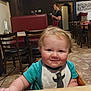 baby, child, high_chair, bib, smile, restaurant, waitress, table, chair, floor, tile_floor, wall, sign, light, red_bench, person, indoor, hair, cute, toddler