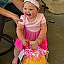Clara joined the competition — help win amazing prizes! toddler, child, pink_dress, headband, toy, yellow_toy, ribbons, smiling, happy, barefoot, adult_hand, outdoor, patio, concrete_floor, chair, person, supporting, cute, playtime, baby