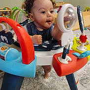 Ky'Son is registered to the contest to win money with this photo: toddler, child, curly_hair, activity_center, toy, indoor, carpet, play, baby, smiling, colorful, furniture, floor, person, young_child, expression, exploration, fun, development, early_learning