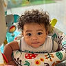 Ky'Son is registered to the contest to win money with this photo: baby, toddler, curly_hair, child, face, eyes, infant, indoor, colorful, toy, baby_activity_center, playtime, cute, young_child, patterned_fabric, expression, portrait, sitting, clothing, closeup