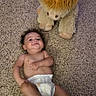 baby, diaper, sock, carpet, stuffed_animal, toy, horns, child, smile, lying_down, indoor, cute, plush, infant, playful, soft_texture, young_child, person, floor, happy