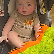 Orion is registered to the contest to win money with this photo: baby, child, car_seat, plush_toy, green, orange, toddler, clothing, rosy_cheeks, indoor, cute, person, smiling, winnie_the_pooh, soft_toy, seat, infant, face, head, comfort