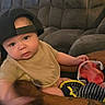 Orion is registered to the contest to win money with this photo: baby, child, bib, cap, sippy_cup, couch, tattoo, arm, indoor, curious, person, hand, clothing, furniture, seated, infant, expression, cozy, casual, home