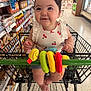 baby, child, shopping_cart, supermarket, grocery_store, toy, plush_toy, curly_hair, smiling, cute, infant, clothing, cheerful, sitting, shopping, aisle, food, store_shelf, footwear, retail