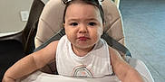 Manuela is registered to the contest to win money with this photo: child, toddler, high_chair, baby, indoor, dining_area, table, chair, hair_bows, white_bib, curly_hair, pout, face, person, floor_tiles, furniture, baby_seat, cute, expression, home
