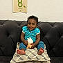 baby, child, couch, cushions, toy, milestone_card, blue_clothing, smile, indoor, wall, patterned_cushions, happy, sitting, infant, feet, face, person, home, decor, cute