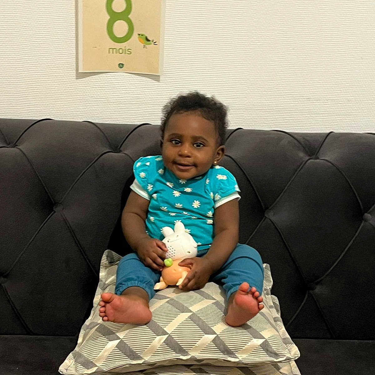 Priscillya a rejoint le concours — aidez-le/la à gagner de superbes lots ! baby, blue_clothing, child, couch, cushions, cute, decor, face, feet, happy, home, indoor, infant, milestone_card, patterned_cushions, person, sitting, smile, toy, wall