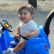 Darian joined the competition — help win amazing prizes! baby, child, toddler, toy_car, blue, smiling, sitting, outdoor, steering_wheel, white_shirt, checkered_shoes, happy, shorts, seat_belt, sunlight, playtime, small_vehicle, young_child, cute, casual_clothing