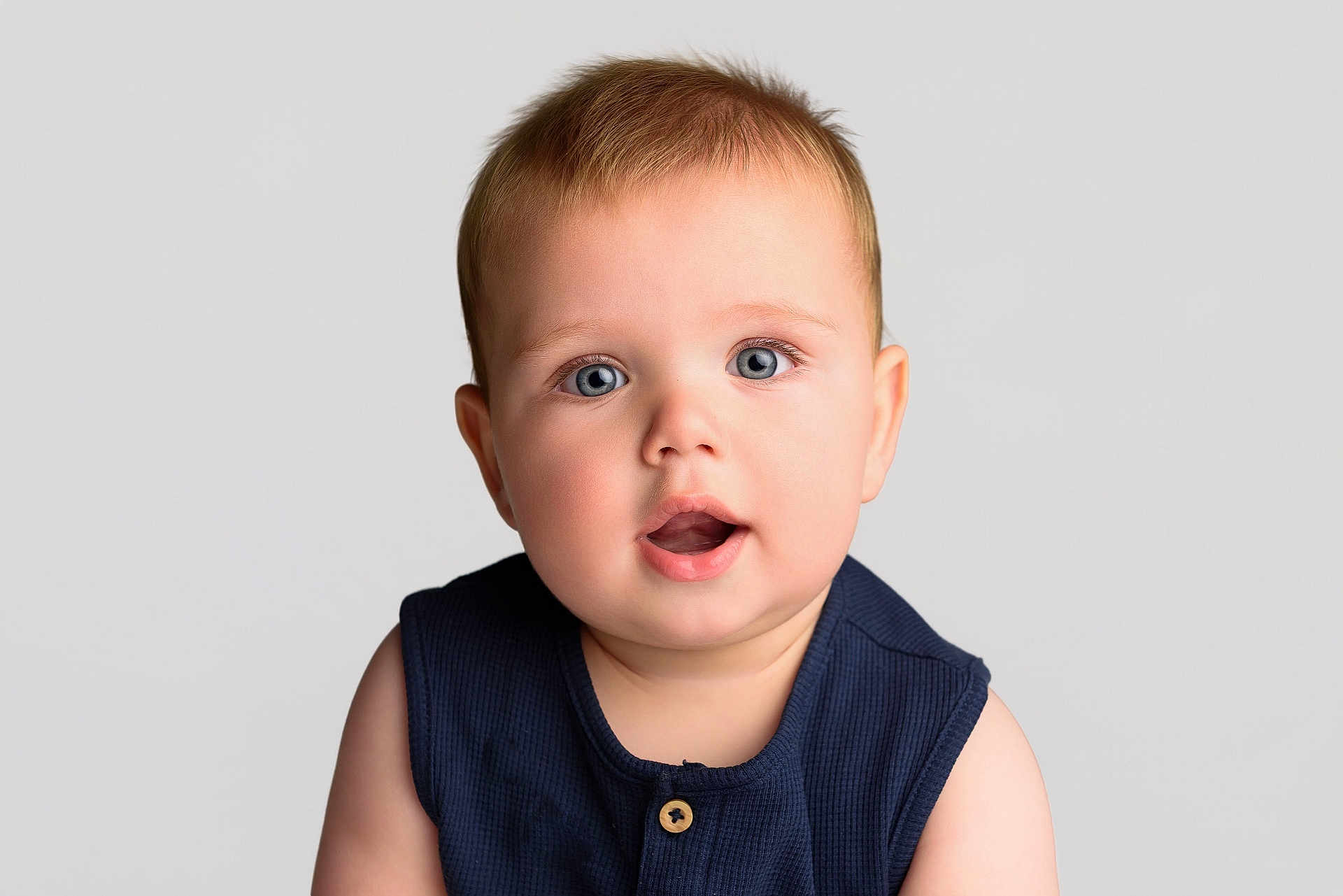Frankie is registered to the contest to win money with this photo: baby, child, face, portrait, blue_eyes, curious, expression, infant, sleeveless_top, navy_blue, soft_skin, close_up, light_background, studio_photo, cute, young, person, head_and_shoulders, innocent, adorable