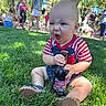 baby, child, grass, outdoor, root_beer, bottle, sitting, expression, summer, park, people, trees, sunlight, shoe, clothing, red_stripes, blue_shorts, casual, funny_face, daytime
