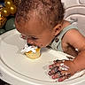 baby, child, infant, eating, cupcake, cake, frosting, messy, birthday, high_chair, tray, hands, curly_hair, portrait, indoors, balloons, celebration, food, smiling, dessert