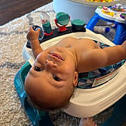 Elijah is registered to the contest to win money with this photo: baby, infant, child, portrait, indoor, playroom, activity_walker, baby_toy, colorful_toys, toy_bin, beads, play_table, rug, carpet, sitting, lying_down, looking_at_camera, face, bare_arms, home