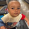 Elijah is registered to the contest to win money with this photo: baby, child, infant, shopping_cart, supermarket, grocery_store, portrait, face, looking_at_camera, serious_expression, indoors, retail, shopping, cart, clothing, shirt, shorts, colorful, close_up, photograph