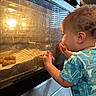 toddler, child, baby, curious, profile, face, person, indoor, kitchen, oven, appliance, warm_light, golden_light, reflection, glass, hands, short_hair, blue_shirt, standing, portrait