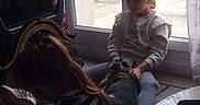 Scoubidou participe au concours pour gagner de l'argent avec cette photo : casual_clothing, child, curtain, dog, floor, glass_door, grass, hair_tied, home, indoor, natural_light, outdoor_chair, petting, plant, relaxed, sitting, striped_shirt, table, white_shoes, window
