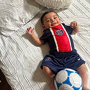 Kassim a rejoint le concours — aidez-le/la à gagner de superbes lots ! baby, smiling, bed, white_bedspread, soccer_ball, sportswear, paris_saint_germain, infant, happy, lying_down, cute, child, indoor, soft_pillow, shorts, toddler, young_child, person, head, hand