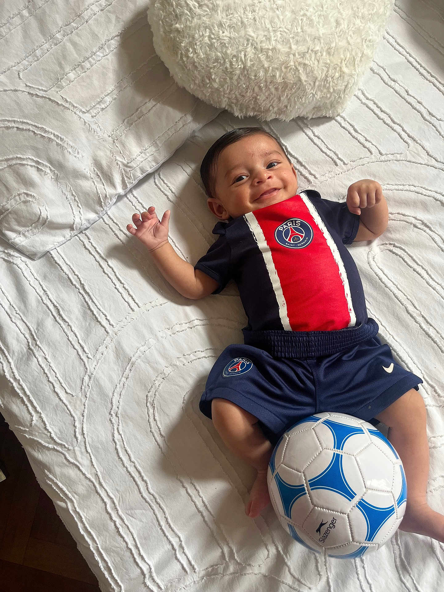Kassim a rejoint le concours — aidez-le/la à gagner de superbes lots ! baby, smiling, bed, white_bedspread, soccer_ball, sportswear, paris_saint_germain, infant, happy, lying_down, cute, child, indoor, soft_pillow, shorts, toddler, young_child, person, head, hand