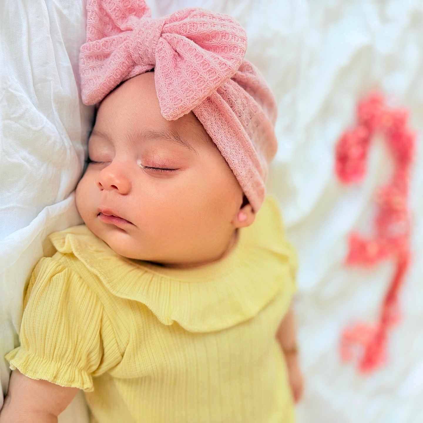 Sophia is registered to the contest to win money with this photo: baby, blurred_background, child, closeup, cute, decor, floral_number, headwrap, indoors, infant, newborn, peaceful, pink_bow, portrait, resting, ruffles, sleeping, soft_fabric, white_background, yellow_dress