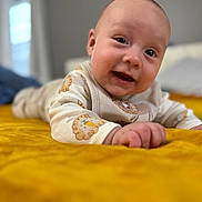 Julian is registered to the contest to win money with this photo: baby, child, smiling, lying_down, blanket, bedroom, yellow, cozy, cute, infant, face, hand, clothing, indoors, portrait, soft_focus, warm_colors, happy, toddler, playful