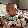 Julian is registered to the contest to win money with this photo: baby, infant, pillow, bed, blanket, clothing, face, hand, skin, room, light, sleeping_area, comfort, curious, portrait, indoor, child, young, soft, peaceful