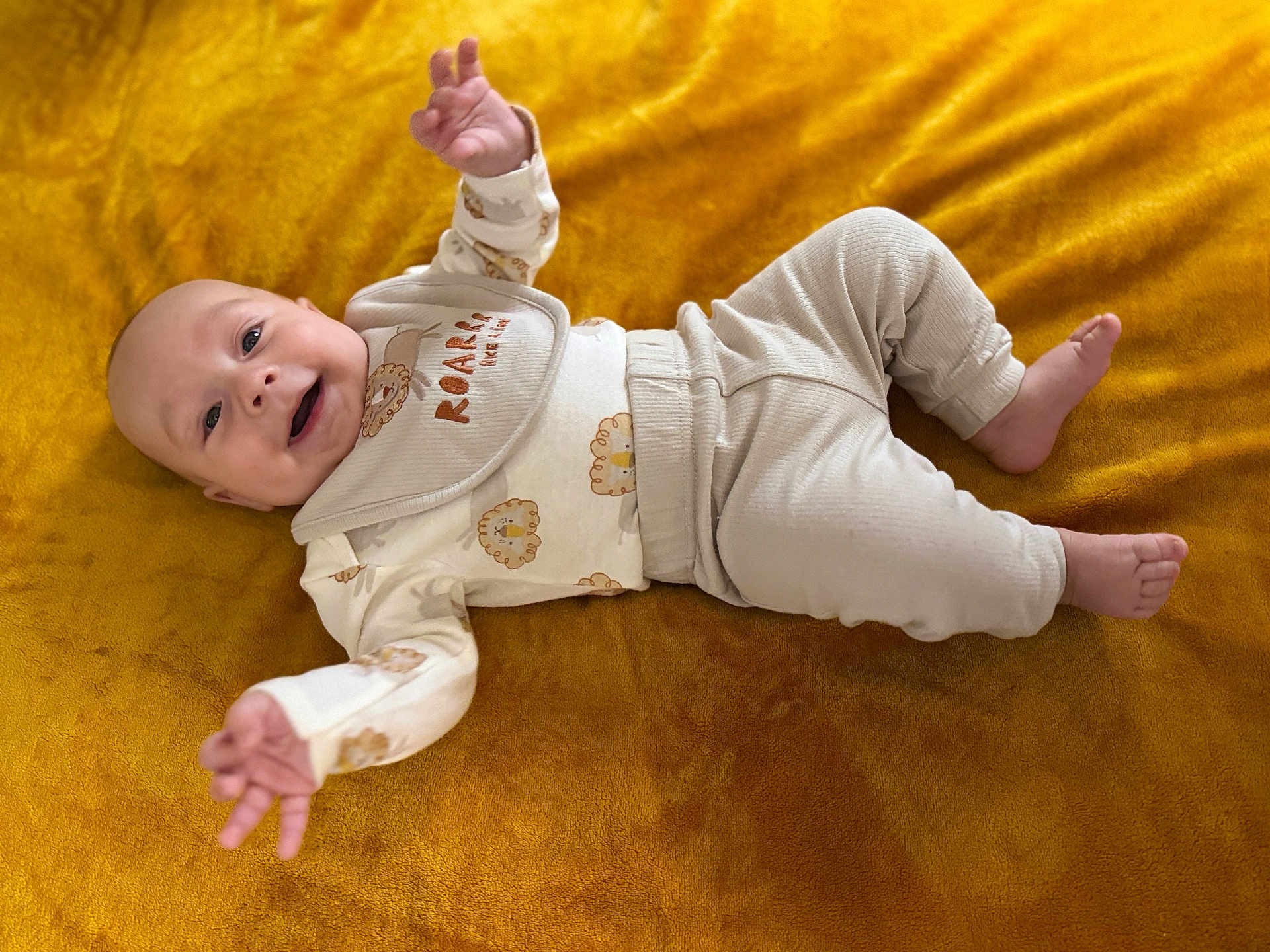 Julian is registered to the contest to win money with this photo: baby, infant, smiling, lying_down, blanket, yellow, pajamas, bib, cute, child, happy, reaching, face, head, skin, foot, hand, clothing, indoors, portrait
