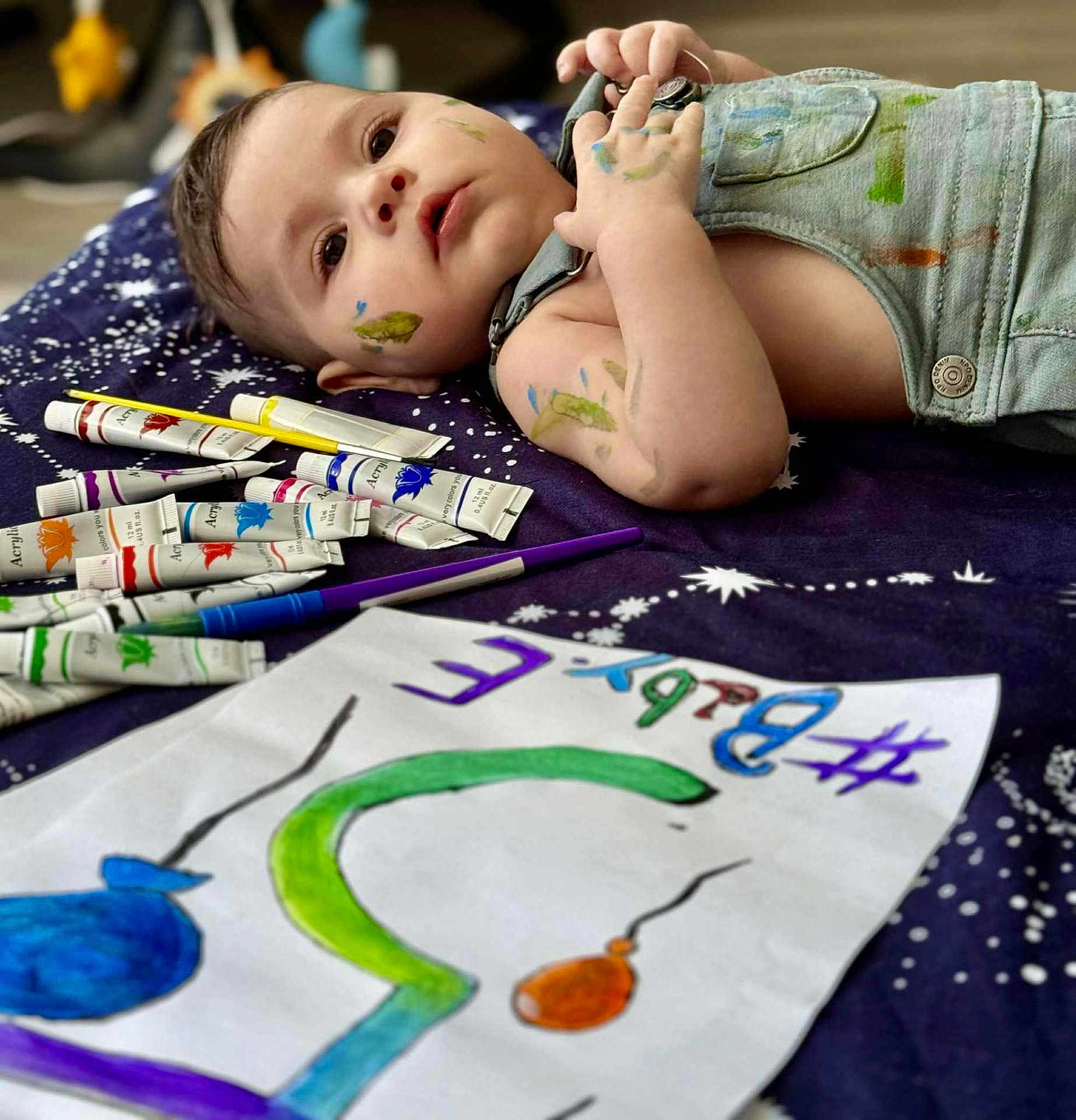 Elis participe au concours pour gagner de l'argent avec cette photo : toddler, baby, face, paint, paint_tubes, paint_brush, artwork, drawing, overalls, blanket, indoor, colorful, messy, child, expression, creativity, hand, paper, closeup, laying_down