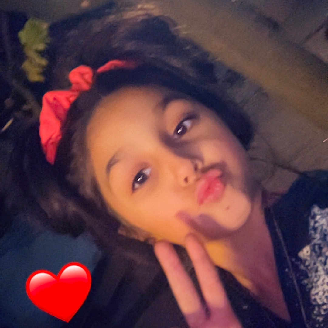 Shainna participe au concours pour gagner de l'argent avec cette photo : casual_clothing, child, dark_background, emoji, expression, face, fun, gesture, girl, hair_accessory, hand_gesture, heart_emoji, indoor, peace_sign, person, playful, portrait, red_bow, selfie, young_person