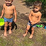 child, boy, barefoot, swim_trunks, outdoor, grass, mud, sunlight, smiling, serious, toy_car, man, walking, stone_wall, path, summer, nature, daylight, play, green_bowl
