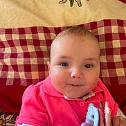 Inaya participe au concours pour gagner de l'argent avec cette photo : baby, infant, child, pink_shirt, teething_toy, blanket, checkered_pattern, floral_design, face, hands, cute, indoors, portrait, smiling, young_child, bright_colors, soft_lighting, close_up, happy, person