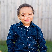Izaiah is registered to the contest to win money with this photo: toddler, child, smiling, portrait, outdoor, blue_shirt, patterned_clothing, curly_hair, happy, sitting, wooden_fence, grass, casual, buttoned_shirt, cute, face, young_child, person, daylight, nature
