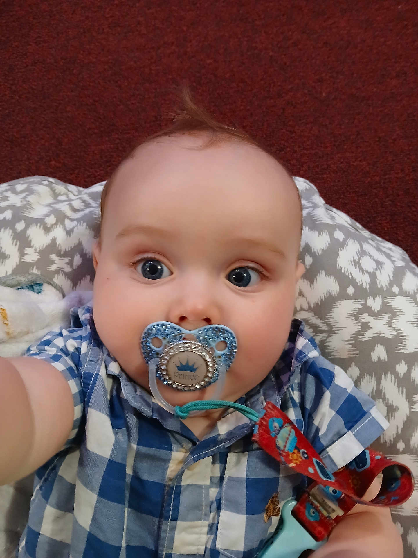Nekoda joined the competition — help win amazing prizes! baby, child, pacifier, blue_eyes, checkered_shirt, close_up, selfie, infant, cute, face, pacifier_clip, patterned_cushion, red_carpet, indoor, plush, wide_eyes, clothing, person, portrait, curious